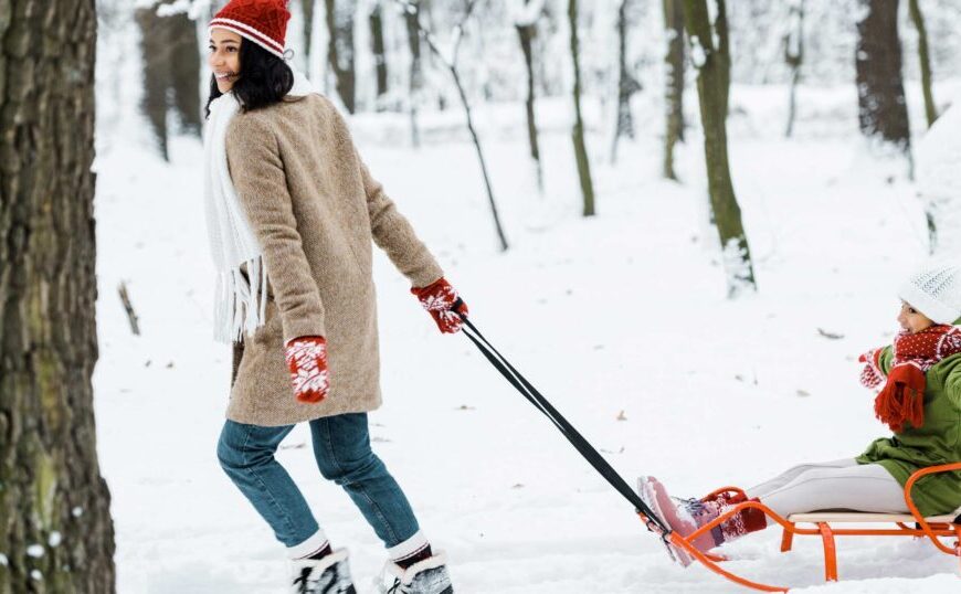 In 2024, a woman leans as she pulls a child on a sled through the snowy landscape.