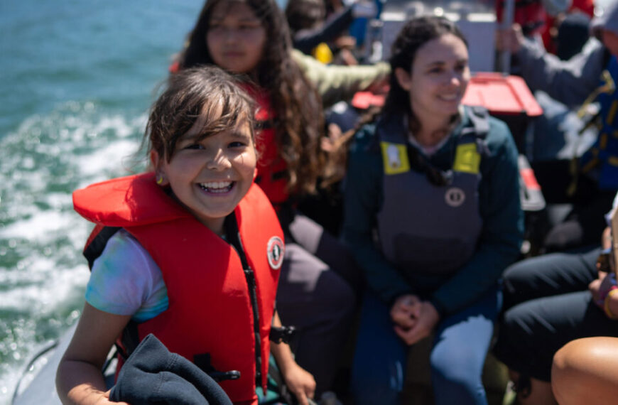 A youth-centred group of people in life jackets on a boat, engaging in place-based learning.
