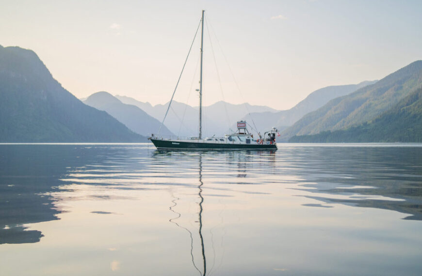 A sailboat sailing in a body of water with mountains in the background, emphasizing conservation efforts.