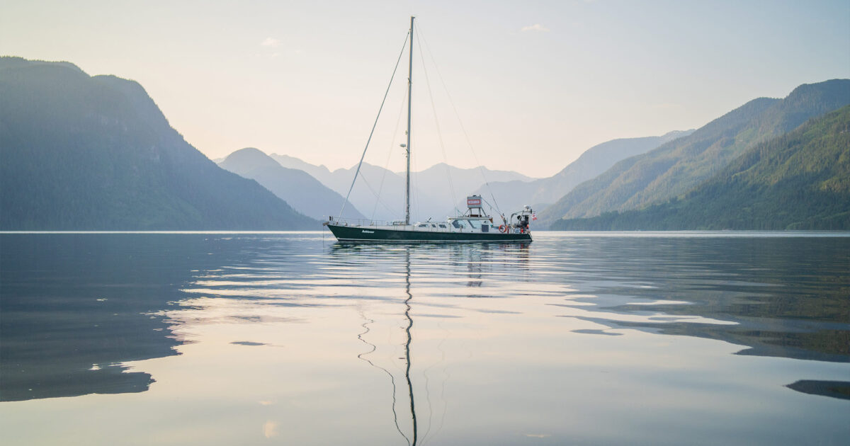A sailboat sailing in a body of water with mountains in the background, emphasizing conservation efforts.