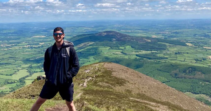A man gracefully stands at the pinnacle of a majestic mountain, soaking in the exquisite vista before him.