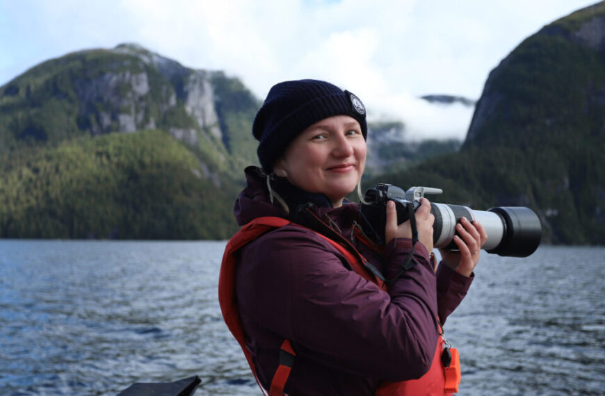 A Postdoctoral Fellow capturing photos on a boat with mountains in the background.