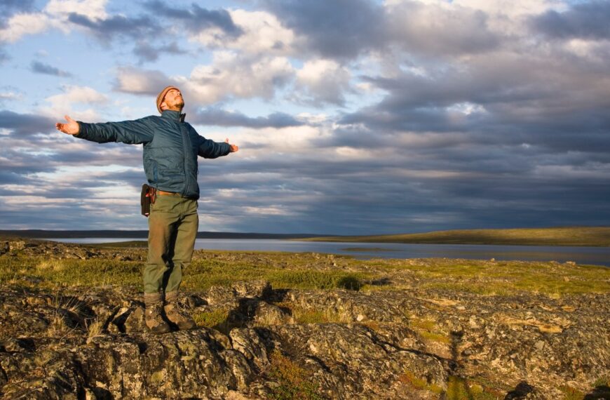 A man standing on a rock with his arms outstretched in the Arctic.