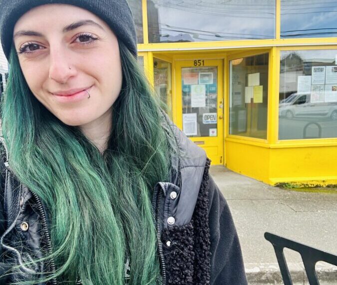 A woman with green hair and a nose ring smiles outside the heart & hands health and well-being collective.