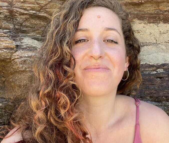 Woman with curly hair smiling in emotional support in front of a rock face.