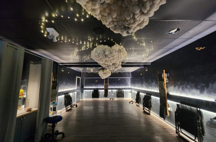A dimly lit room with cloud-like decorations and string lights on the ceiling, dark walls, a wooden floor, and various pieces of equipment stored along the walls. The bespoke details hint at a recent Reno done by H&H experts.