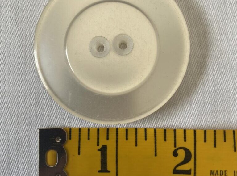 Large clear plastic button next to a measuring tape, indicating the diameter is approximately 1.5". Perfect for projects requiring large buttons that measure around 2 inches or less.