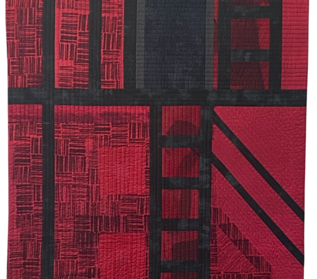 A red and black quilt depicting the abstract image of The Annex with a large doorway, a ladder in the center, and geometric patterns throughout.