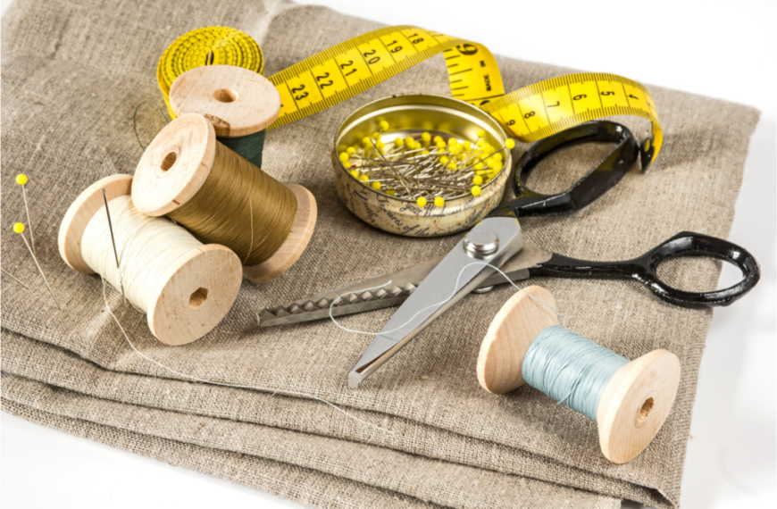 A behind-the-scenes glimpse: A sewing kit with thread spools, scissors, measuring tape, and a tin of pins placed on fabric.