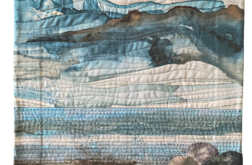 A quilted landscape artwork depicting endless horizons with mountains, tranquil water, and a rocky shore. The design is enriched with shades of blue, brown, and white accented by intricate stitching patterns.