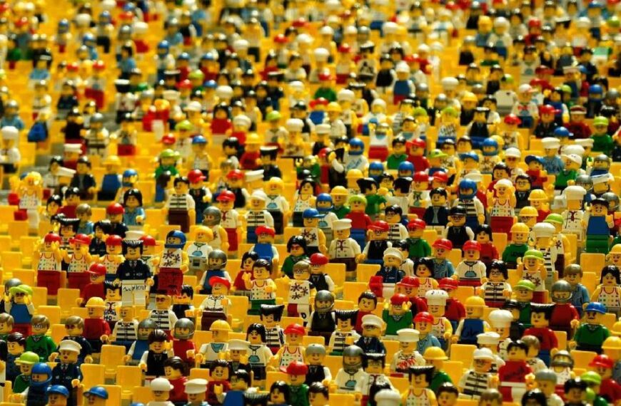 A large crowd of colorful LEGO minifigures, each with unique outfits and accessories, tightly packed together in rows, resembling a lively scene during conference season.
