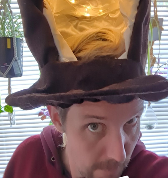 Person wearing a large, brown top hat with a yellow interior and lights, standing indoors. Text reads "Next layer of crafting." It's the perfect ensemble for STICC Halloween, blending creativity and flair for the spooky season.