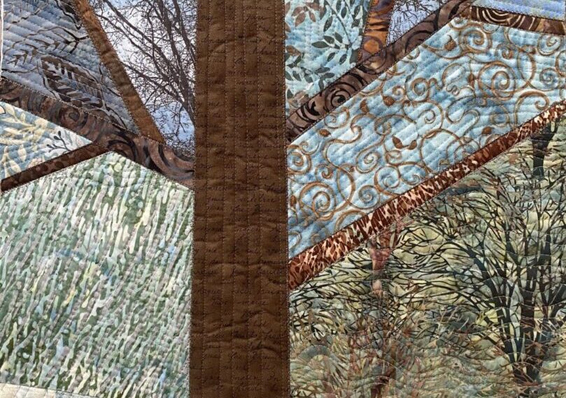 A quilt features a central brown tree trunk with radiating branches, surrounded by various patterned fabrics resembling tree branches and leaves. The patterns give a layered, textured effect, creating an intricate landscape that evokes the majesty of trees on a mountain.