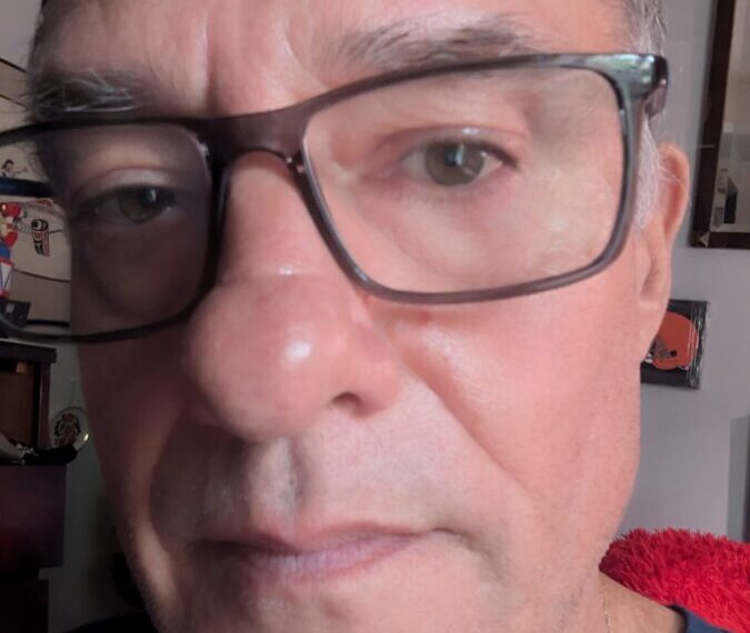 A close-up of a person wearing glasses, looking at the camera with a neutral expression, subtly showing the quiet resolve of healing in their eyes.
