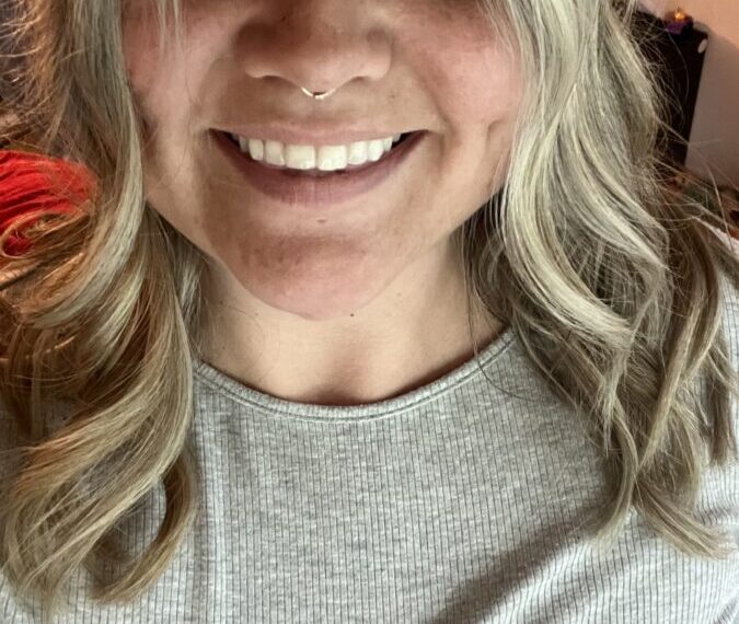 Selfie of a person with light-colored hair, wearing a gray ribbed shirt and smiling at the camera, their eyes reflecting a deep sense of gratitude.