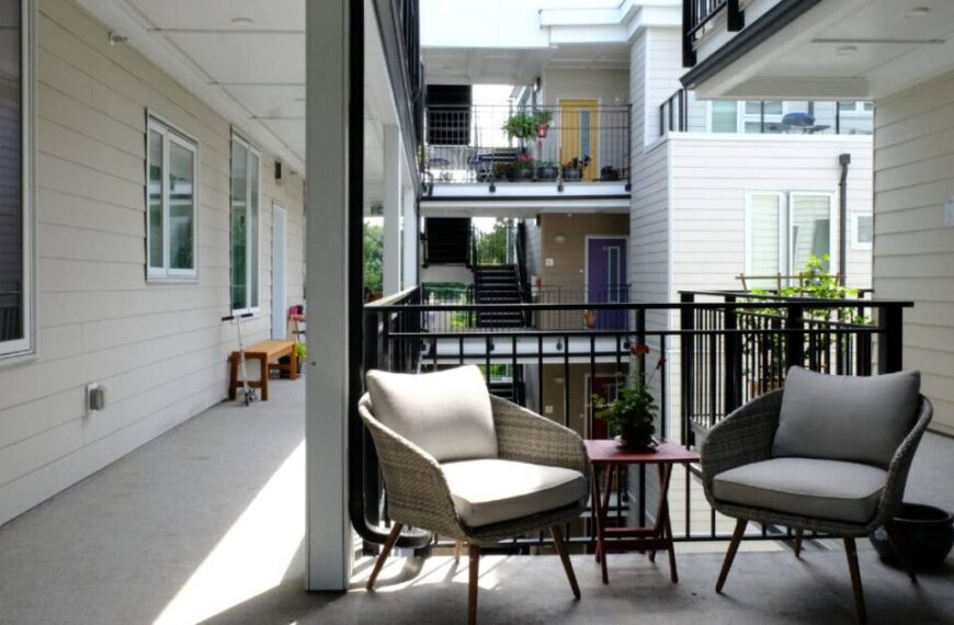 Two cushioned chairs and a small table on a sunny apartment balcony with potted plants create the perfect spot for relaxation, blending home improvement with social design to enhance your living space's charm and functionality.