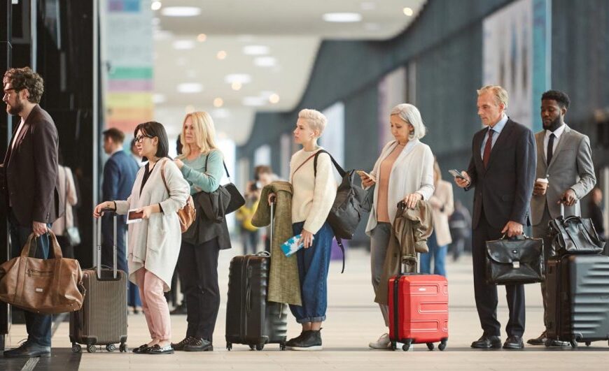 A diverse group of people stands in line with luggage, eagerly anticipating their travel adventures at the airport.