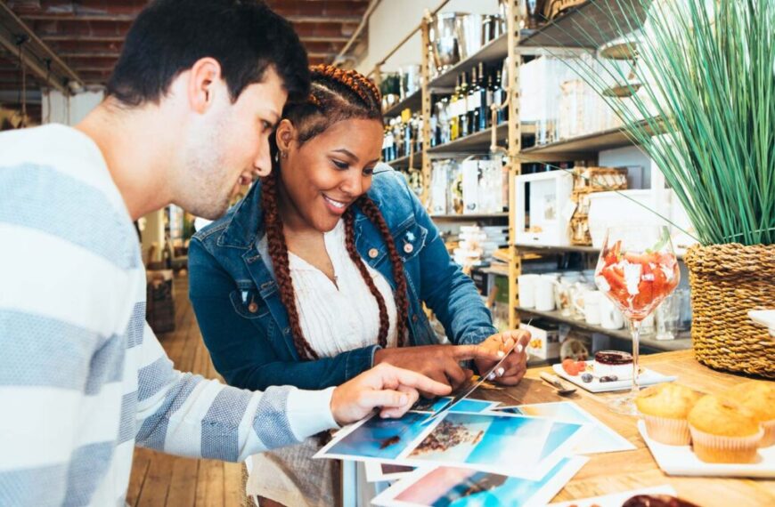 Two people, with the keen eye of successful entrepreneurs, are absorbed in travel photos laid out on a table in a shop. Their emotional intelligence shines through as they share stories and insights sparked by each image.