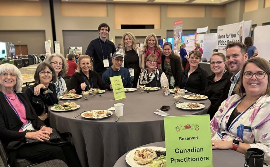 A group of people sits around a table with food under a sign reading "Reserved Canadian Practitioners" at the ILADS 2024 conference, discussing advances in tick-borne disease research.