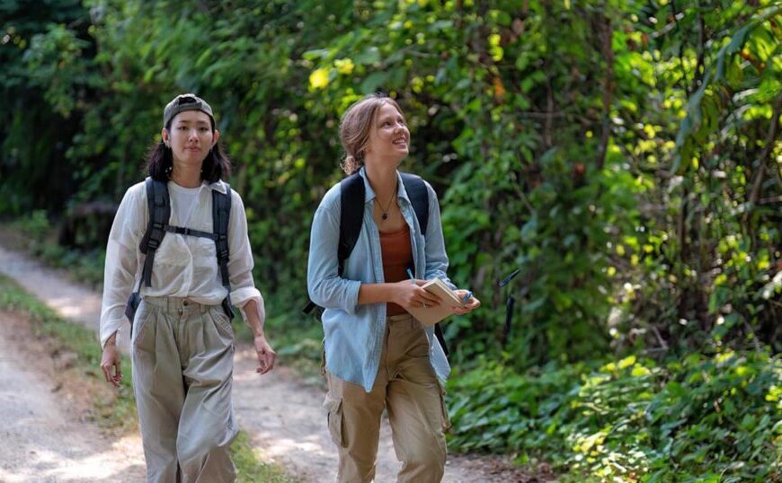 Two people walking on a forest path, carrying backpacks and maps, are surrounded by lush green foliage. They've treated their gear with Permethrin as a prevention measure against tick-borne infection, ensuring a safe and enjoyable trek through nature's beauty.