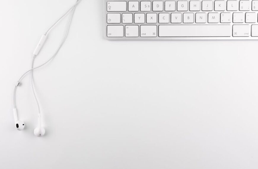 On a white surface, white earphones lie gracefully beside a silver keyboard, ideal for university students using text-to-speech technology.