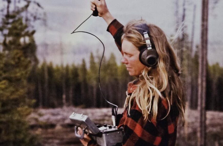 In Episode 1, Diane Boyd, wearing a plaid shirt, uses a handheld radio device with headphones to track the progress of gray wolf recovery in a forested area.