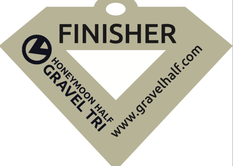 Revealing the diamond-shaped finisher medal for the Honeymoon Half Gravel Tri, featuring the event logo and website: www.gravelhalf.com.