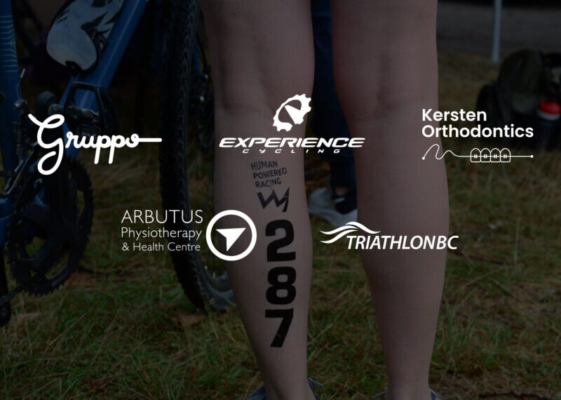 A person stands next to a bicycle with race number 287 marked on their calf, surrounded by multiple sponsor logos at the 2025 Cowichan Challenge—perfect for the community photo album.