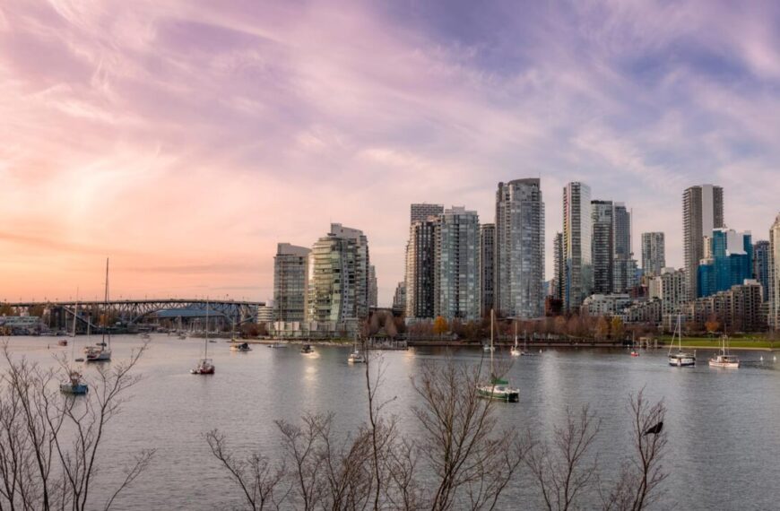 City skyline with modern high-rise buildings along the False Creek waterfront, several boats on the water, and bare trees in the foreground under a partly cloudy sky at sunset—a setting often featured in collaborative studies of water quality.