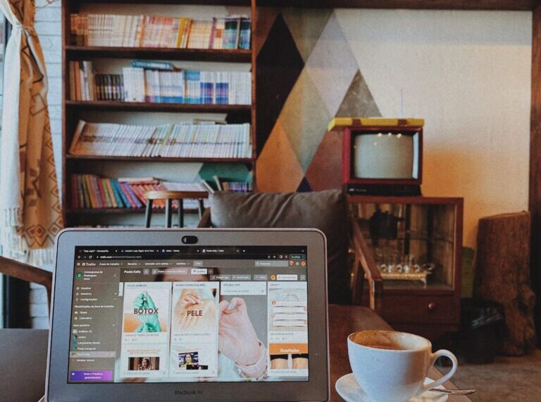 A laptop displaying a WordPress webpage sits on a wooden table next to a cup of coffee in a cozy room with bookshelves and a vintage TV in the background.