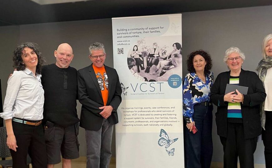 Six people stand in front of a VCST banner, smiling for a group photo in an indoor setting during the Interconnectedness Initiative year in review.