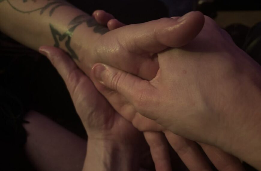 Close-up of one person massaging another's forearm and hand, focusing on a tattoo near the wrist—capturing a quiet moment that hints at a desire to undo tension and offer comfort.