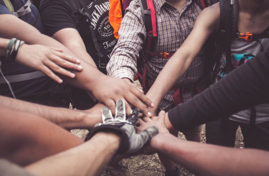 A group of people, some with backpacks and outdoor clothing, join their hands together in the center, united in support of ISH and CHC Funding.