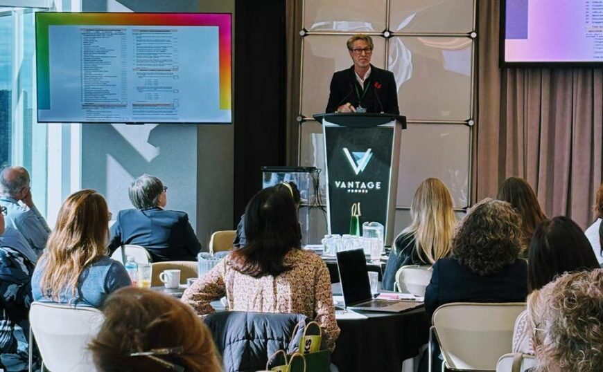 A speaker presents at a podium labeled "Vantage" in front of an audience, with slides about Canadian Tick-Borne Disease displayed on two screens in a conference room.