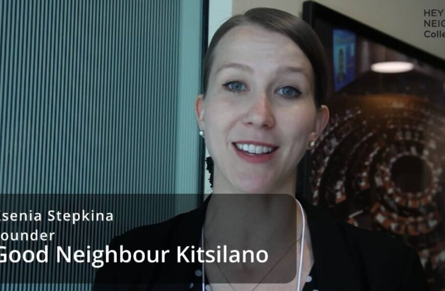 A woman stands indoors, smiling at the camera during an interview. A text overlay reads, "Ksenia Stepkina, Founder, Good Neighbour Kitsilano." A logo in the corner says "HEY NEIGHBOUR! Collective.