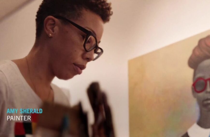 A person with glasses stands beside a painting of a person with red glasses. Text on the image reads "Amy Sherald, portrait artist.
