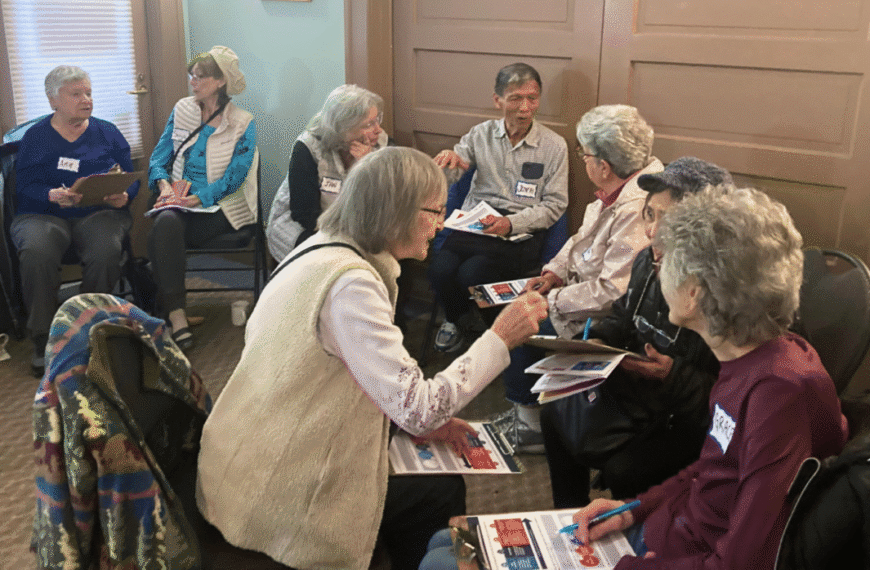 A group of older Canadian adults sit in two small circles, talking and holding papers and booklets in a room with beige walls and a window—a wonderful partner highlight moment.