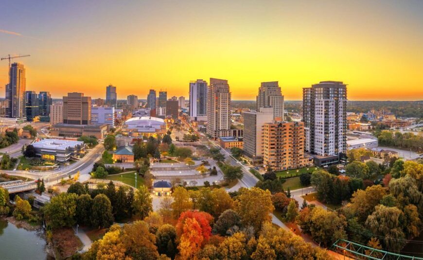 Aerial view of a city skyline at sunset with tall buildings, roads, parks, and autumn trees in the foreground—an evocative glimpse into how urban design in Canada is increasingly shaped by climate-health considerations.