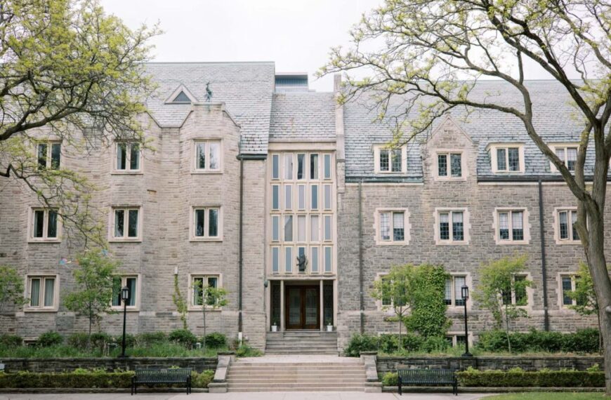 A stone building with multiple windows, an arched entrance, and a staircase, surrounded by trees and benches on a cloudy day—an inviting setting where students gather to discuss everything from campus life to the latest scholarship opportunity.