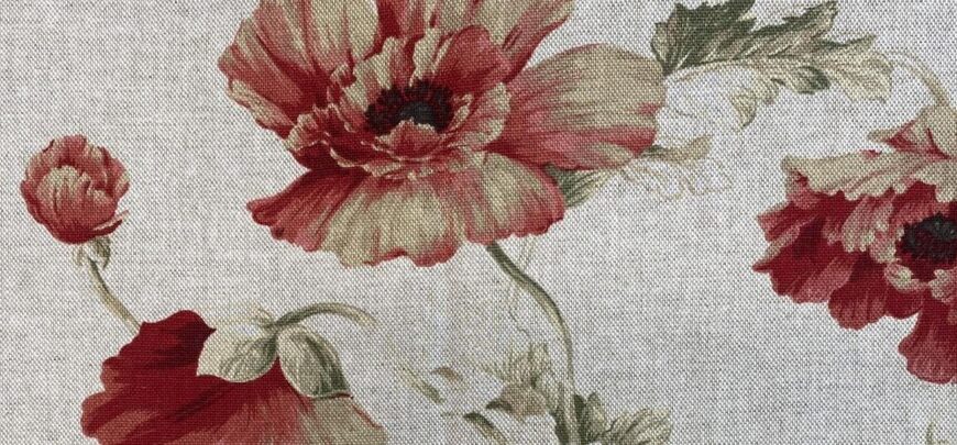 A chair upholstered in fabric with a pattern of red poppy flowers and green leaves on a light gray background.